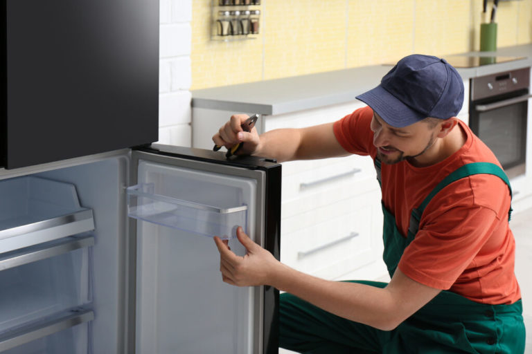 Male technician with pliers repairing refrigerator indoors